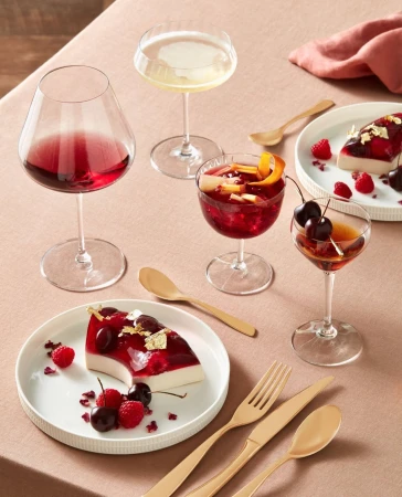Arrangement of dessert plates and stemmed glasses filled with colorful drinks and desserts on a beige tablecloth.
