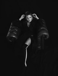 Kim Cattrall seated in a large leather armchair in a black trench coat for Numero Netherlands, photographed by Fernando Sippel