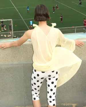 Woman in yellow top and polka dot leggings standing before a soccer stadium viewed from above