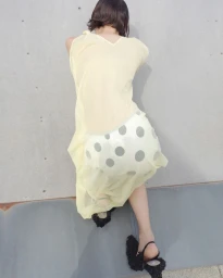 A person in a pale yellow dress leaning against a concrete wall wearing black textured sandals