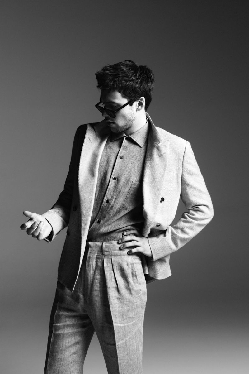 Monochrome portrait of stylish adult man wearing a gray suit with open shirt, posing confidently in a photo studio against a gray backdrop.