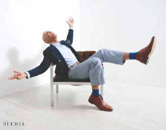 Bald man laughing with arms outstretched seated in a chair against a white background for Photobook Magazine