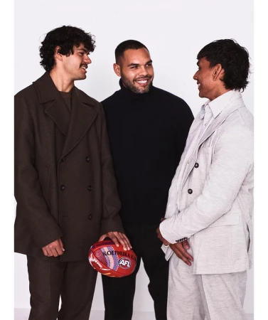 Three adult males in a photo studio wearing fashionable jackets and sweaters posing with an Australian Rules Football (AFL) football.