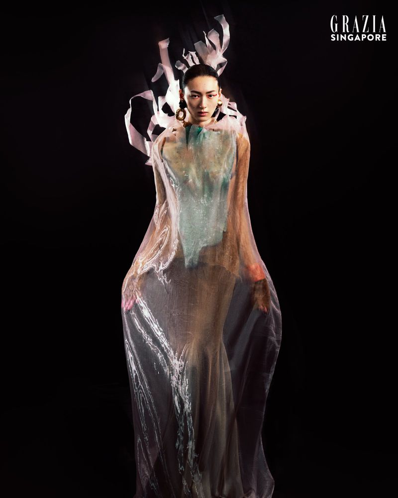 Fashion editorial shot of a woman in an elaborate iridescent gown with a dark background, featured in Grazia Singapore, showcasing a unique style.