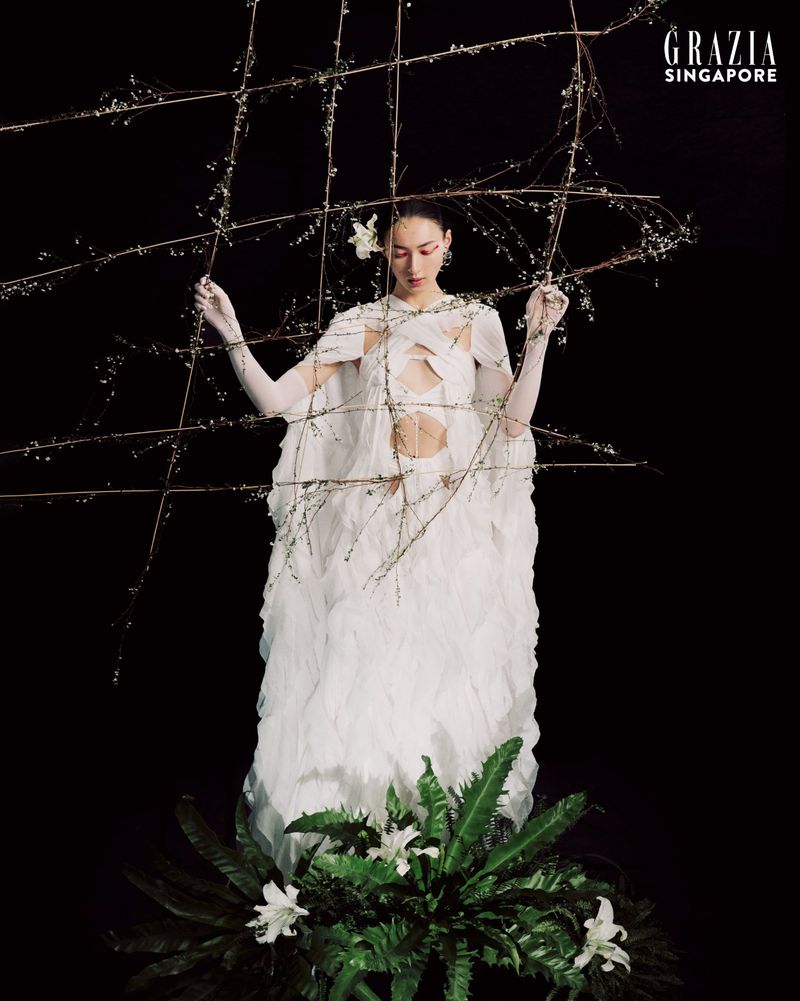 Fashion editorial image of a woman in a feathered dress posing with botanical elements against a black backdrop for Grazia Singapore.