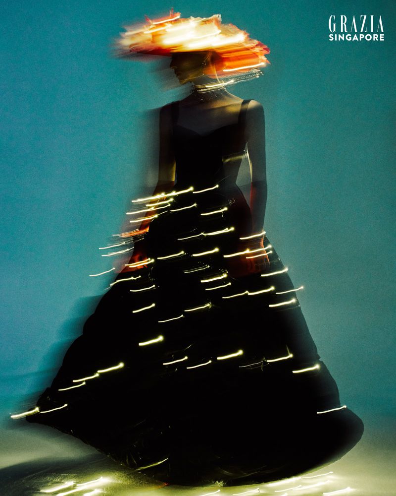 Fashion shot: Blurred woman in black dress and orange hat in a studio, shot with long exposure and studio lighting for a blurred effect.