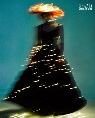 Fashion shot: Blurred woman in black dress and orange hat in a studio, shot with long exposure and studio lighting for a blurred effect.
