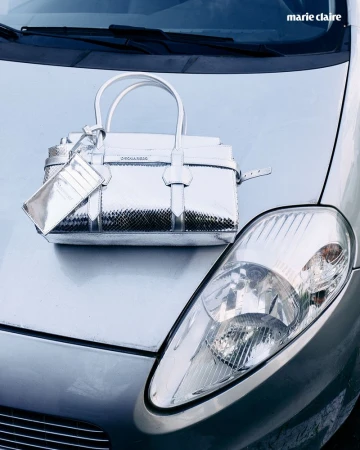Metallic silver handbag on the hood of a silver car, with a visible headlight and the logo of Marie Claire magazine.