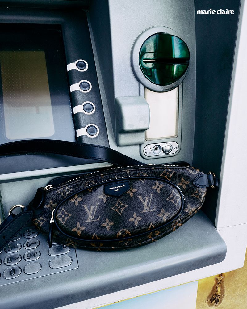 A stylish brown Louis Vuitton belt bag is resting on the keypad of a grey ATM machine with the Marie Claire logo visible above.