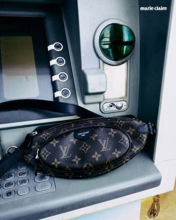 A stylish brown Louis Vuitton belt bag is resting on the keypad of a grey ATM machine with the Marie Claire logo visible above.