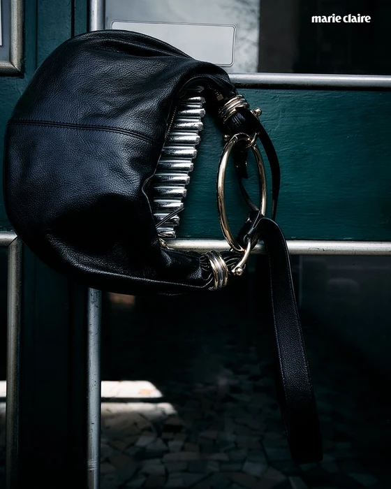 Black leather handbag with silver hardware hanging on a dark green door for Marie Claire U.S. still life project