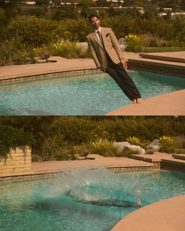 Man in suit leaps into a swimming pool, creating a splash. The scene is set outdoors against a backdrop of greenery and clear skies.