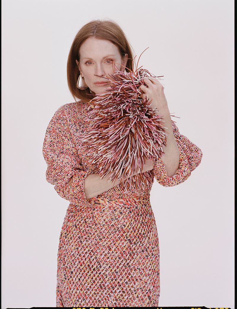 Portrait of a red-haired woman in a patterned dress, holding a textured ball, against a white background in a studio setting.