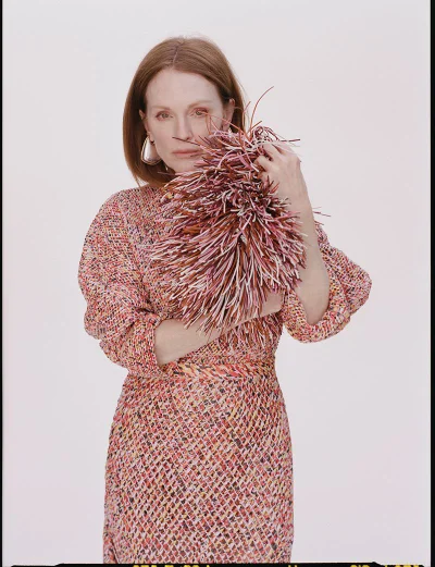 Julianne Moore holding a textured fringed accessory wearing a patterned dress against a plain white studio background.