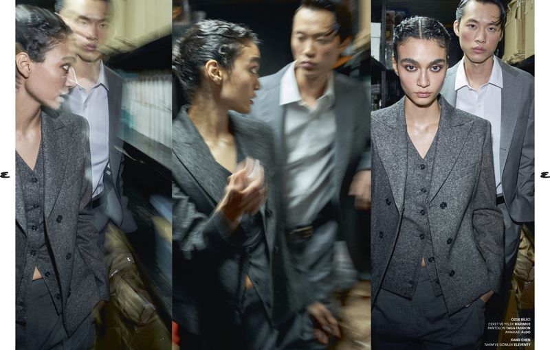 Fashion editorial shot featuring an Asian male and female posing in gray suits against a blurred background. Soft, natural lighting.