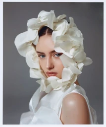 Model Leni Klum wearing a white floral headpiece and matching white top against a grey seamless background