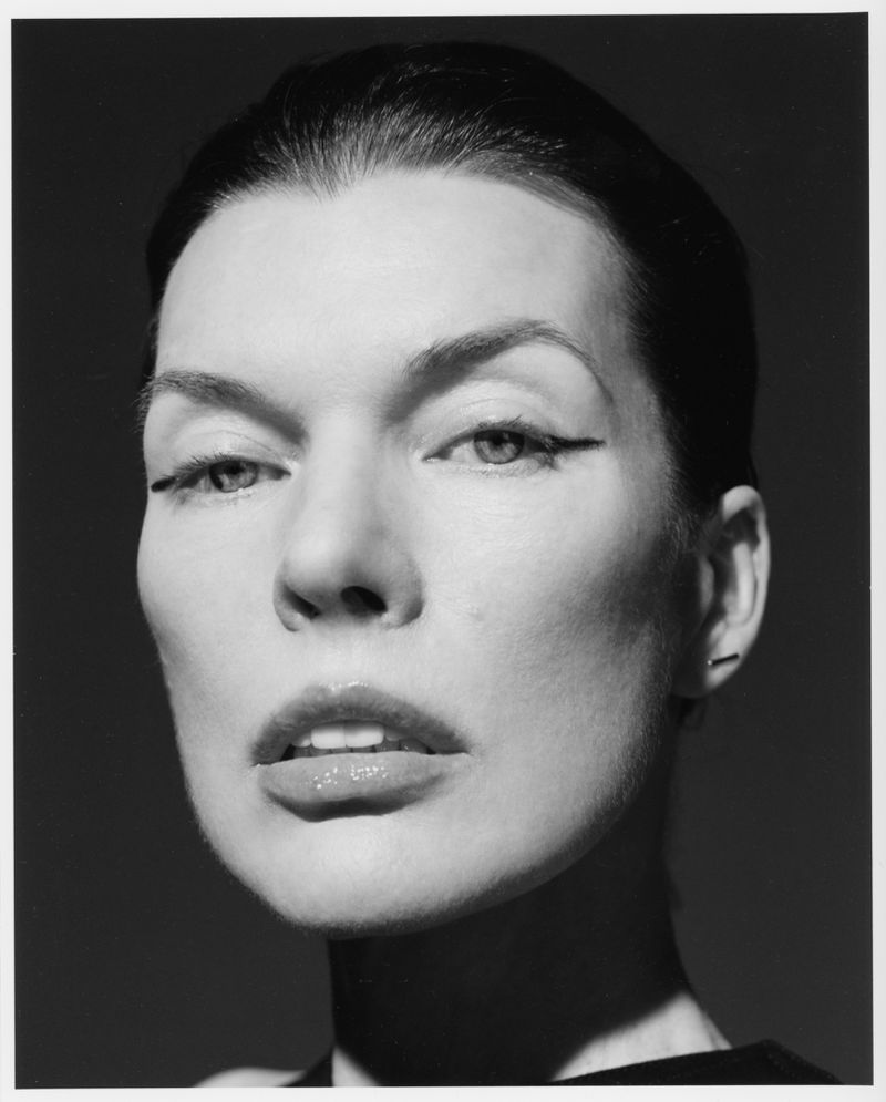 Black-and-white close-up portrait of an adult female with clean makeup, dramatic eyeliner, and glossy lips against a dark background.