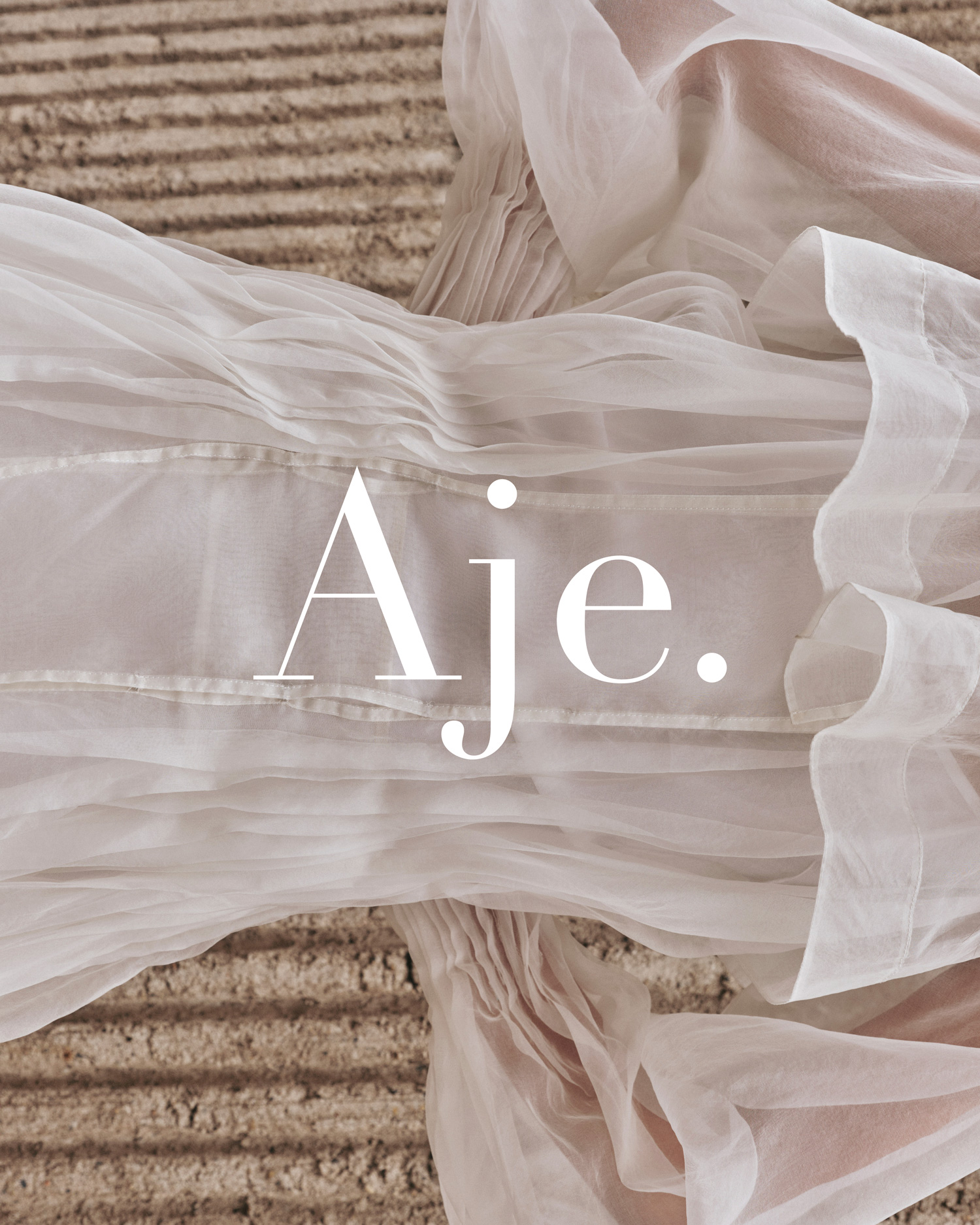 Close-up of a layered, sheer white dress with textured fabric and the Aje logo overlaid, creating a soft and elegant fashion image.