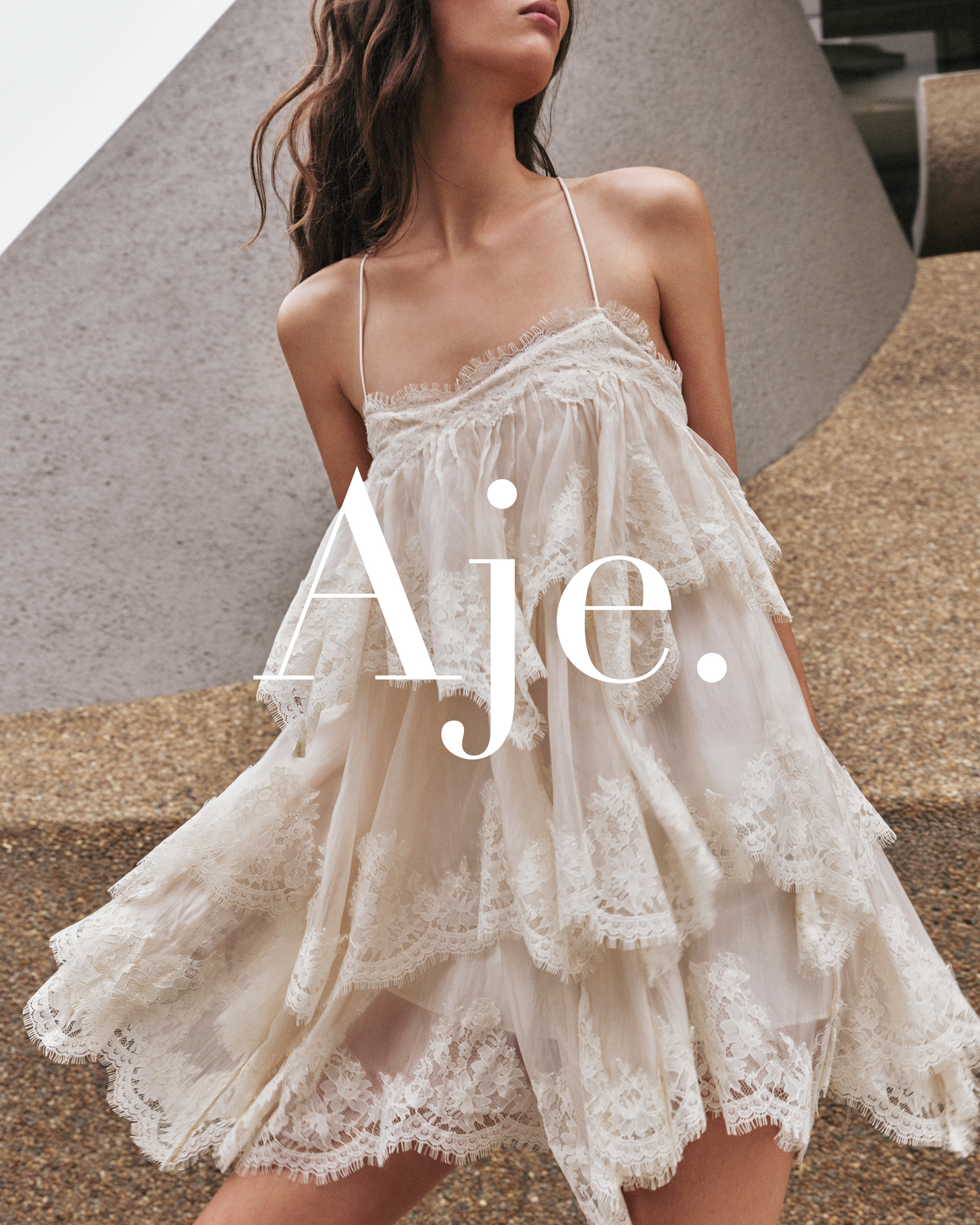Woman models a tiered, lace-trimmed mini dress by Aje in a studio fashion shot with natural lighting and minimalist background.