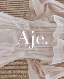 Close-up of white sheer ruched fabric with textured carpet background and bold Aje logo overlay