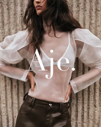 Model in white sheer organza top and dark brown leather pants against a textured stone wall