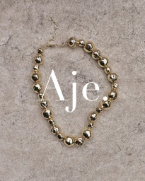 Gold beaded statement necklace arranged in an organic loop against a textured grey stone surface