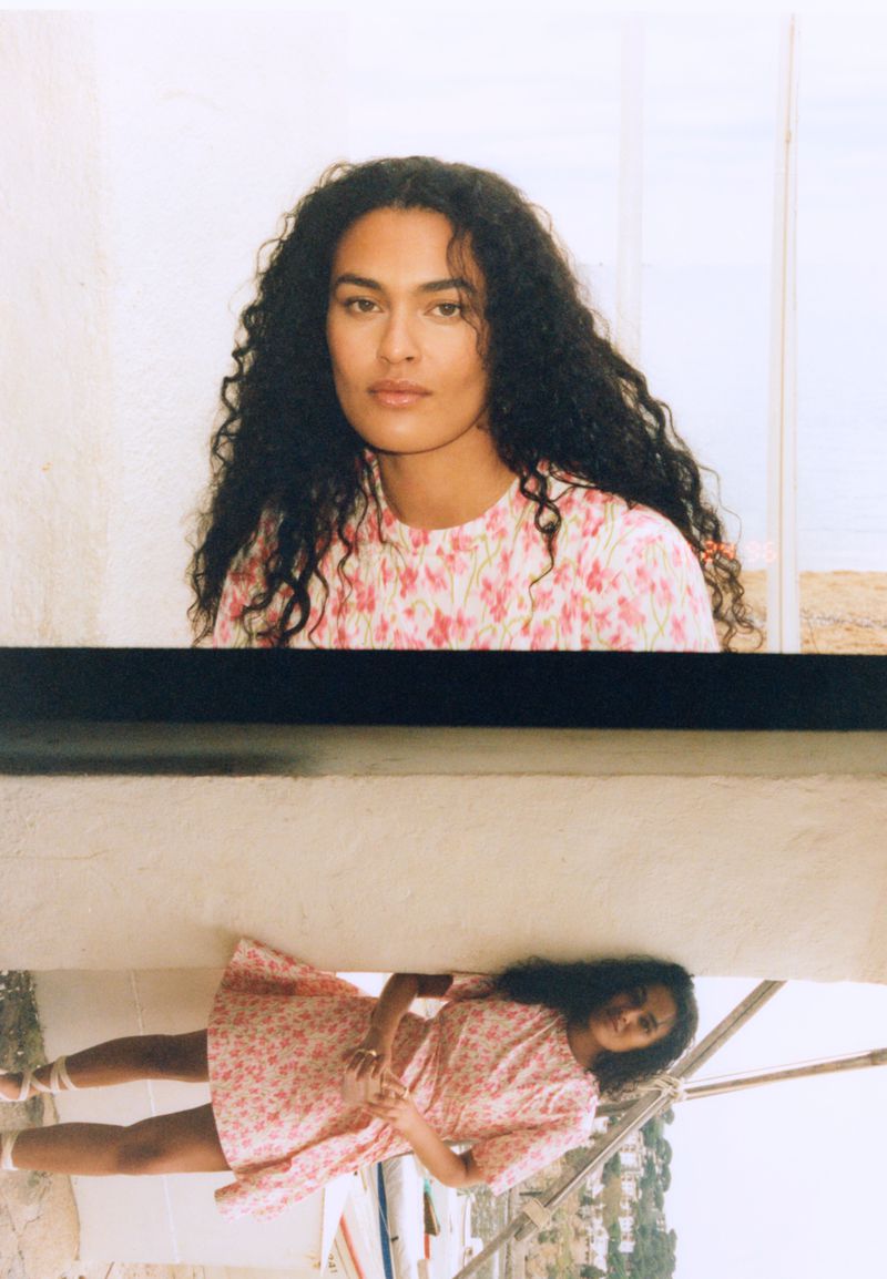 Attractive woman in a pink floral dress poses outdoors with an unusual perspective and reflection on a white surface.