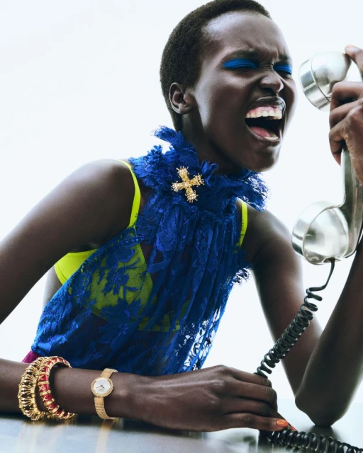 Dramatic portrait of an African-American woman screaming into a retro telephone, showcasing a blue lace top and vibrant makeup.