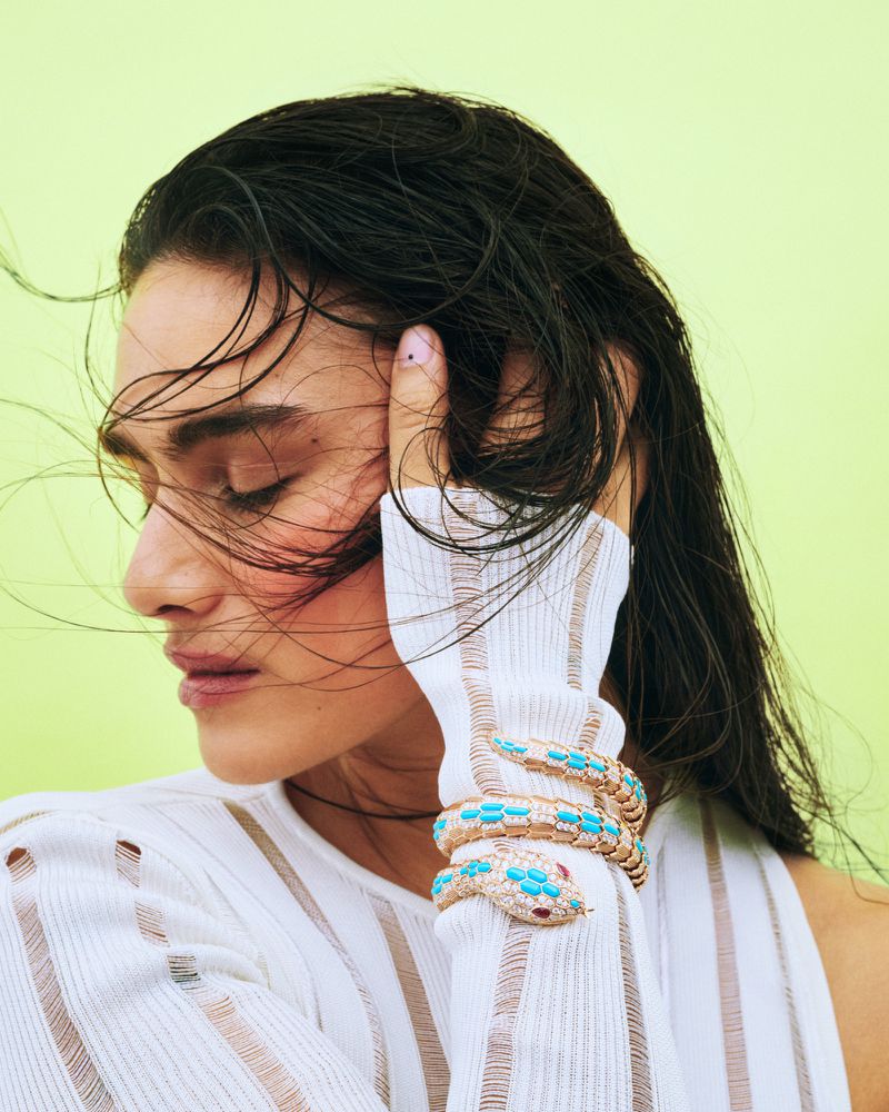 Woman with dark hair and fair skin, wearing a white top and a golden snake-shaped bracelet with turquoise stones, in a studio shot.