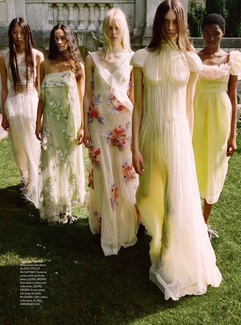 Five women in sheer dresses stand in a row outdoors, with a classical building in the background. Fashion editorial photoshoot.