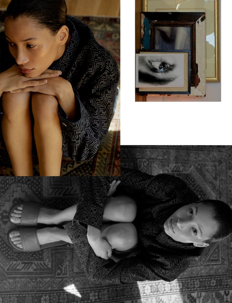 Woman in patterned robe sitting on patterned rug, seen from above, with framed artwork in the background, indoor natural lighting.