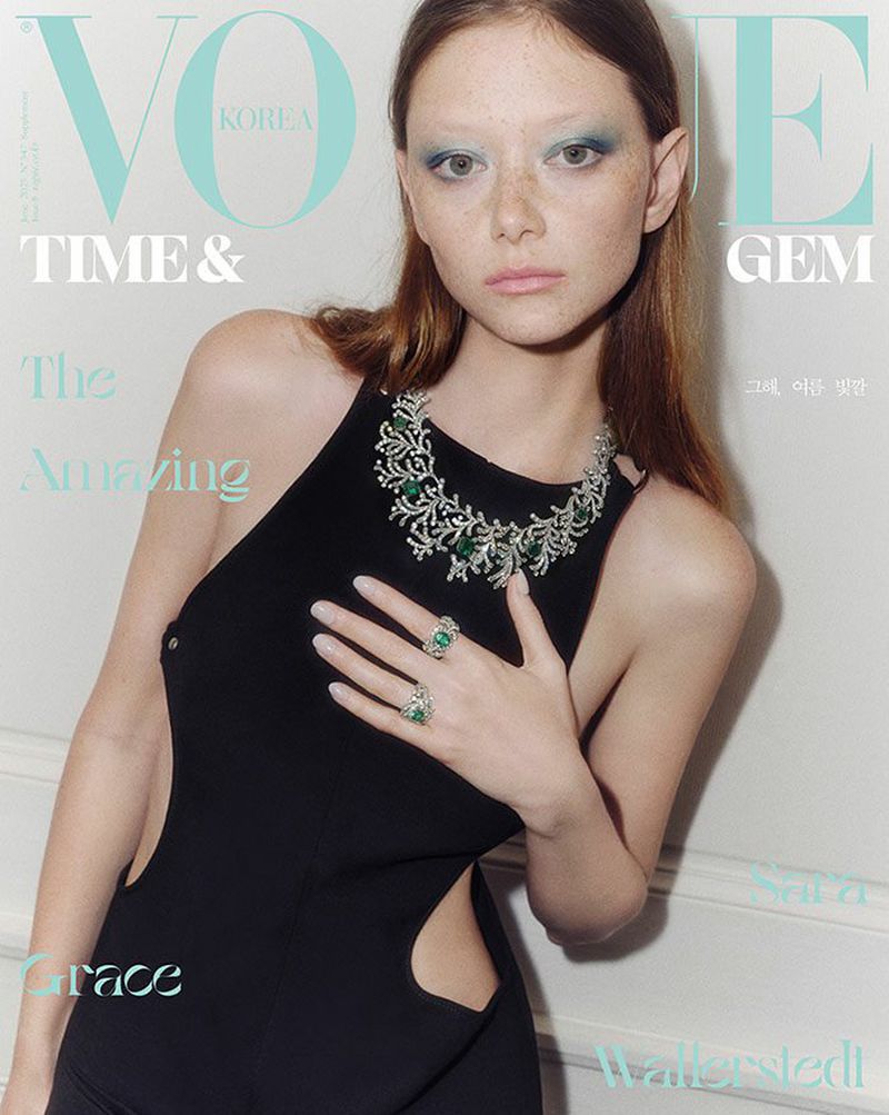 Magazine cover featuring a fair-skinned model in a black dress wearing emerald and diamond jewelry, posing in front of an off-white wall.