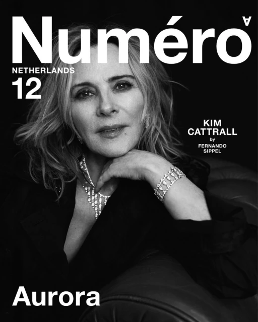 Black and white magazine cover shot of Kim Cattrall wearing diamond jewelry and a black blazer against a dark background. 