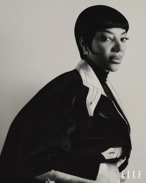 Monochrome portrait of a woman with short black hair wearing a jacket; an ELLE magazine logo is visible in the lower right corner.