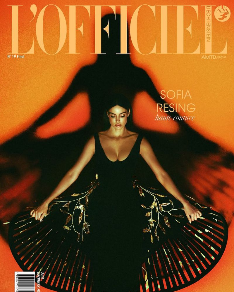Magazine cover featuring a woman in a black dress with gold leaf detail, posed against a warm orange background with a shadow.