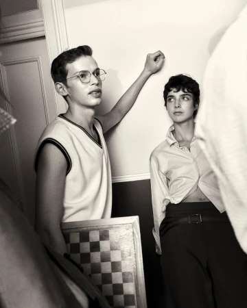 Monochrome portrait of a young adult couple posing indoors against a white wall, featuring a checkerboard and vintage aesthetic.