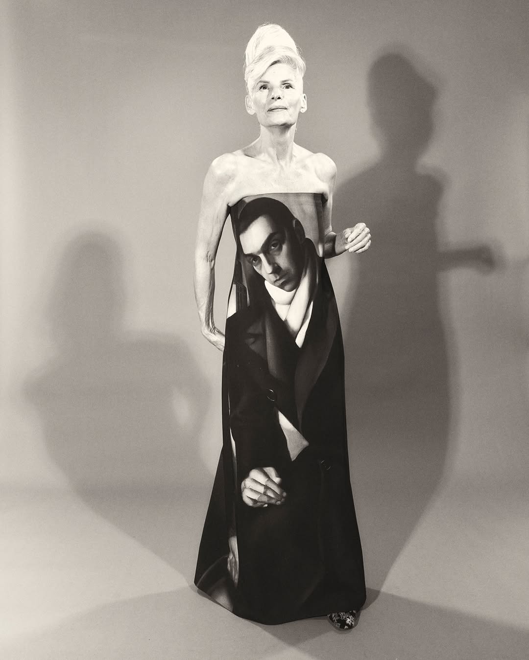 Artistic studio shot of an older woman in a monochrome palette, wearing a unique dress printed with a vintage man's portrait.