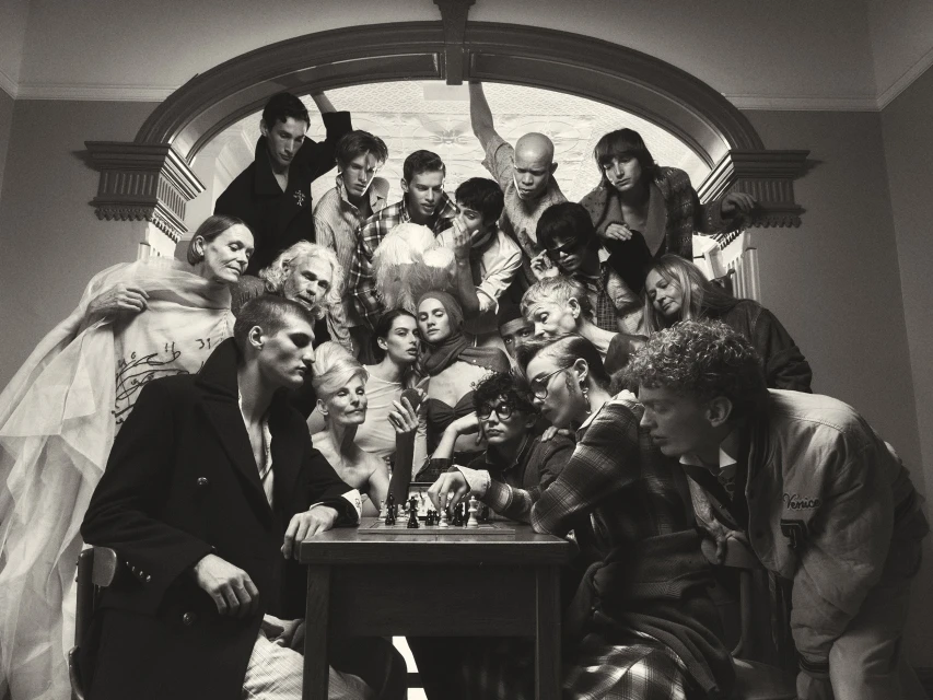 Group of diverse people gathered around a table playing chess under an arched doorway for COAT Magazine Chess Club editorial