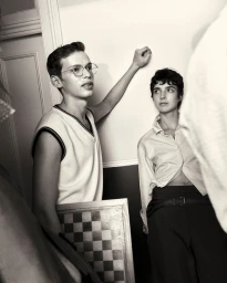 Two models standing indoors near a wall, one holding a chessboard for COAT Magazine project Chess Club