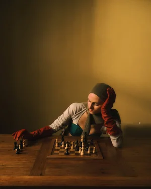 Woman in red leather gloves leaning over a wooden chess board in a warmly lit room for COAT Magazine Chess Club editorial