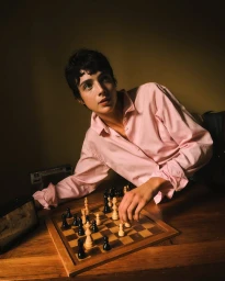 Person in a pink button-down shirt leaning over a wooden table playing a game of chess for COAT Magazine