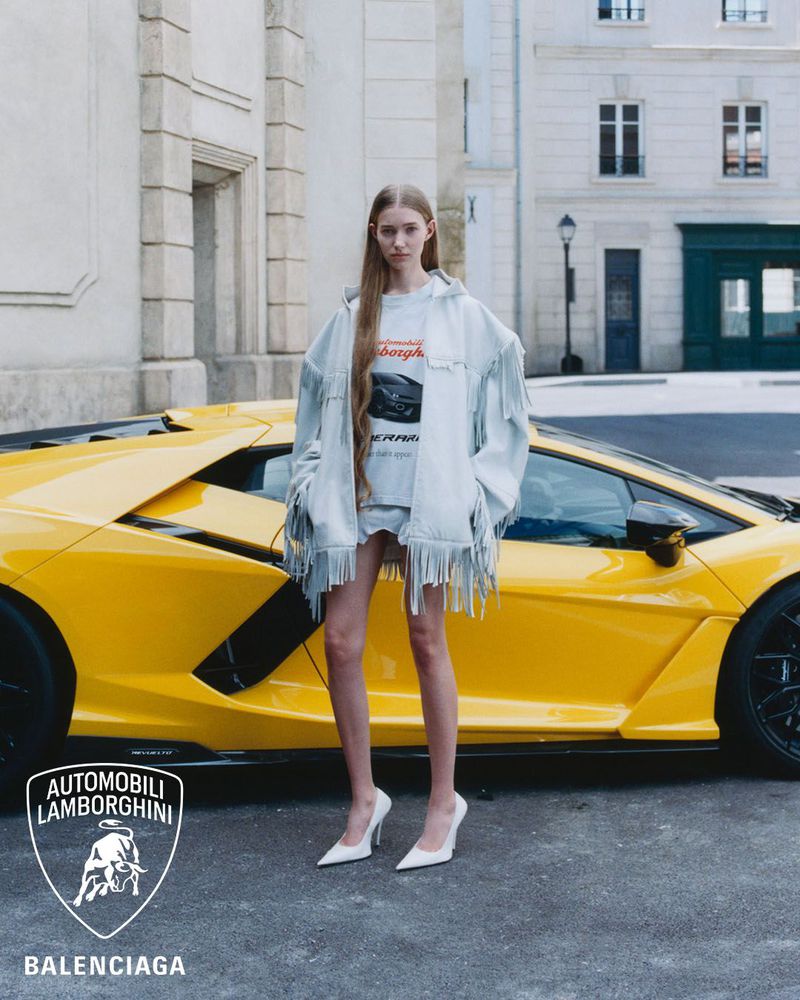 Fashion shot of a young, fair-skinned woman posing by a yellow Lamborghini, wearing a white t-shirt, denim jacket, and white heels in an urban setting.