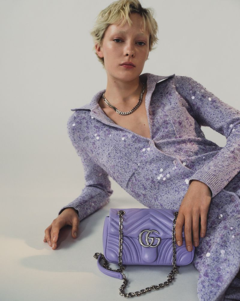 Woman poses with lilac Gucci Marmont handbag in a studio. The model is wearing a collared lilac sweater dress with silver necklace.