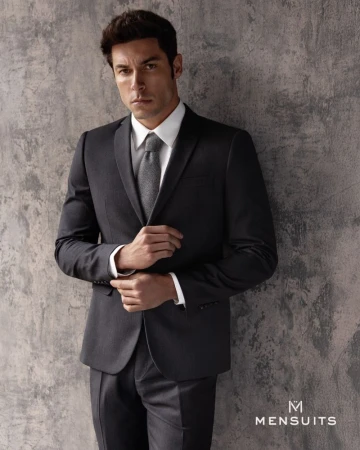 Portrait of handsome adult male in a dark business suit leaning against a textured wall wearing a white dress shirt and gray tie.