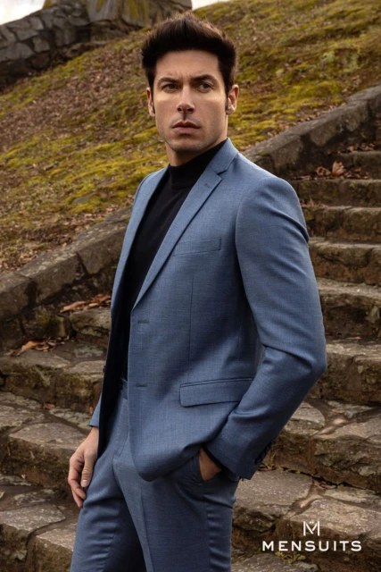 Portrait of an adult man in a blue suit standing on stone steps outdoors with foliage in the background, looking slightly to the left.