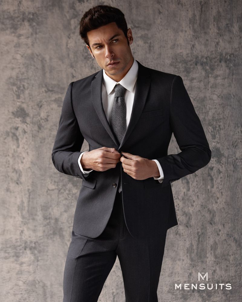 Portrait of adult male wearing suit and tie while posing against a grey textured backdrop in a studio setting. Menswear fashion shot.