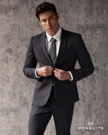Portrait of adult male wearing suit and tie while posing against a grey textured backdrop in a studio setting. Menswear fashion shot.