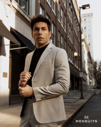 Model Andrea Denver wearing a light grey suit and black turtleneck on a city street for Mensuits.com SS25