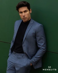 Model wearing a blue suit and black turtleneck leaning against a green wall for the Mensuits.com SS25 campaign.