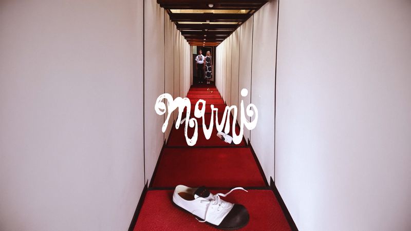 Fashion editorial shot in a hallway with a white and black shoe, two figures in the background and the Marni brand logo.